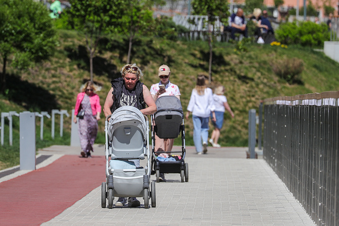 Женщина с ребенком в детской коляске гуляет по городскому парку