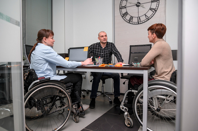 Женщины в инвалидных колясках общаются с сотрудником офиса