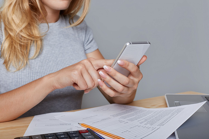 Девушка со смартфоном в руках, на столе счета и калькулятор 